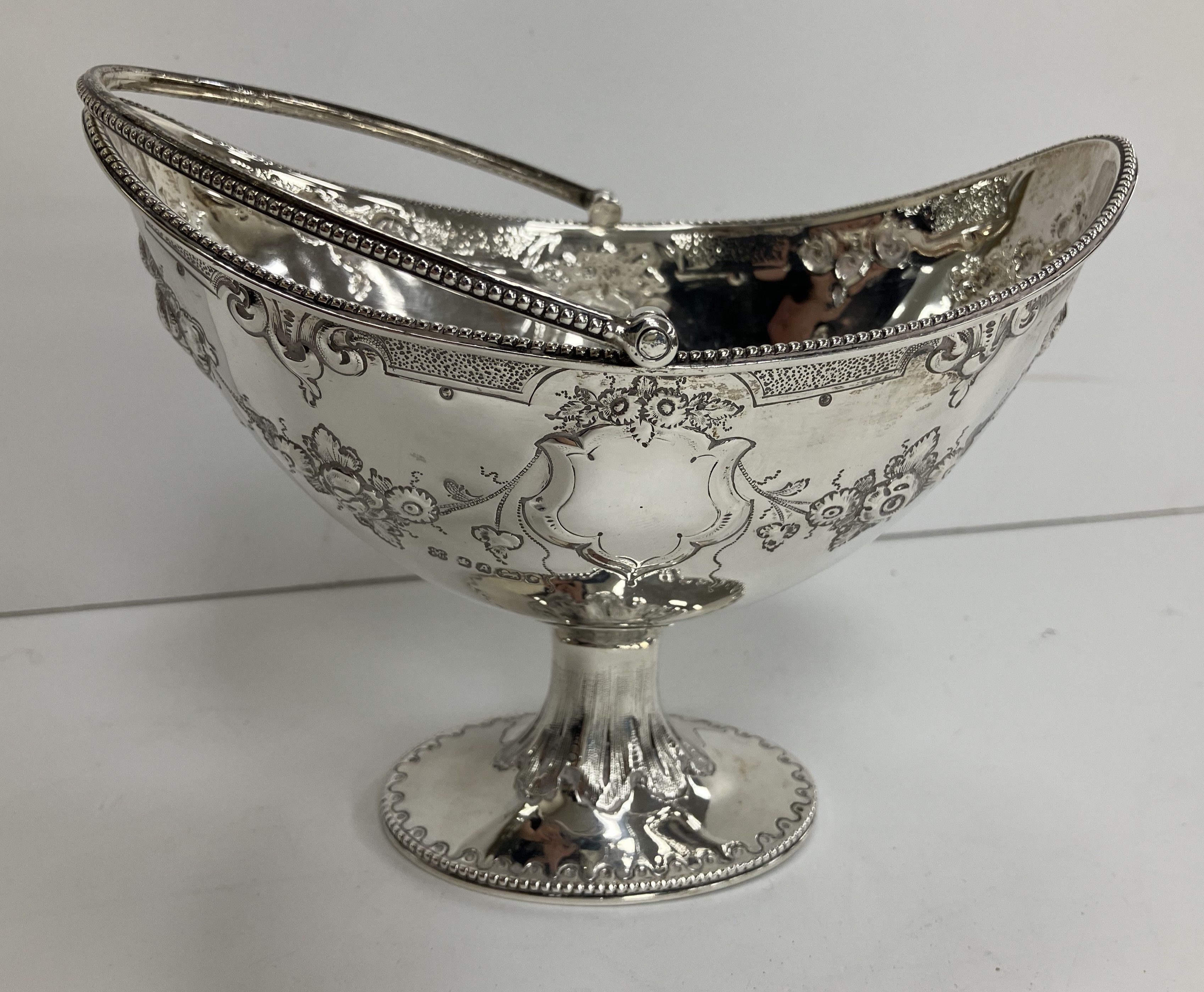 A Victorian silver sugar basket of navette form with beaded edge and swing handle over a fruit and