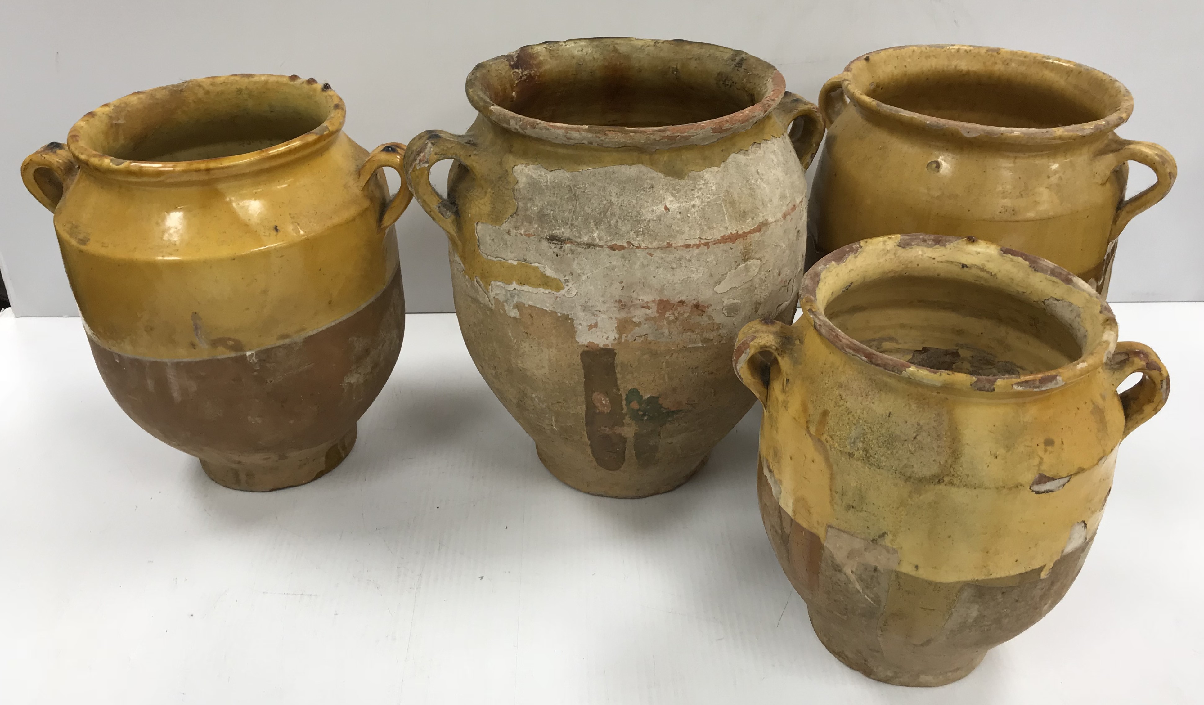 A collection of four 19th Century and later French ochre part glazed confit pots with lug handles,