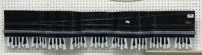 A glass wall sculpture of a grand piano keyboard and cover, signed in gold to right, 