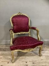 A Victorian style gilt armchair having an encircling frame, red fabric upholstered back and seat, on