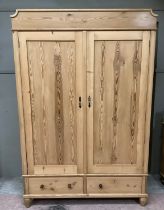 A pine wardrobe with a shaped pediment, two doors above two short drawers on bun feet, 136cm wide