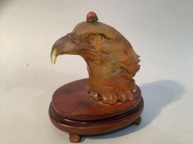 A Chinese amber coloured glass eagle head snuff bottle, mounted on a stand, 11.5cm high