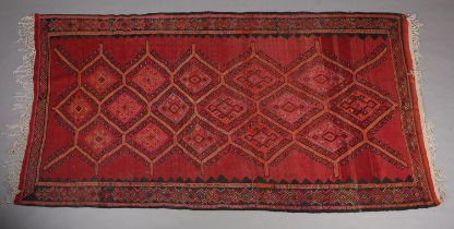 A Middle Eastern carpet, the wine ground filled with a panel of multiple diamond motifs, filled with