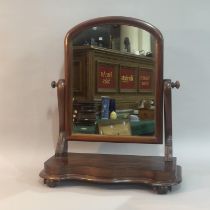 A Victorian mahogany toilet mirror having an arched glass, serpentine uprights and on scrolled feet,