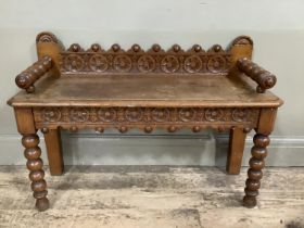 An oak hall bench with bobbin arms and legs, heavily carved back and carved apron