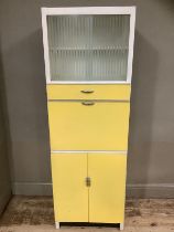 A mid century yellow formica kitchen table with a glazed unit above drop down cupboard