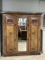 A Victorian walnut triple wardrobe with carved cartouches, pediment top, central mirrored door,