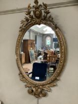 A gilt ornate oval wall mirror having a shield pediment with applied foliate moulding, 95cm high