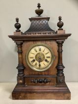 A German heavily carved wooden clock with pitched roof and urn finials, HAC movement, enamel dial