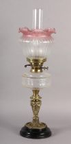 A VICTORIAN BRASS OIL LAMP, clear glass reservoir, cranberry tinted opaque shade etched with