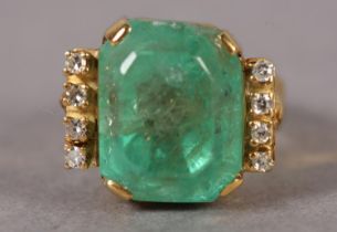 AN EMERALD AND DIAMOND RING IN 9ct gold, the step cut emerald claw set flanked by eight cut diamonds
