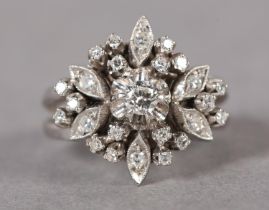 A DIAMOND CLUSTER RING, c1965, claw set to the centre with a brilliant cut stone raised against a
