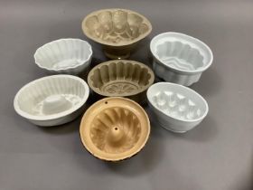 Seven white and buff pottery jelly moulds and one painted with leaves and flower heads on a brown