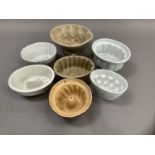 Seven white and buff pottery jelly moulds and one painted with leaves and flower heads on a brown