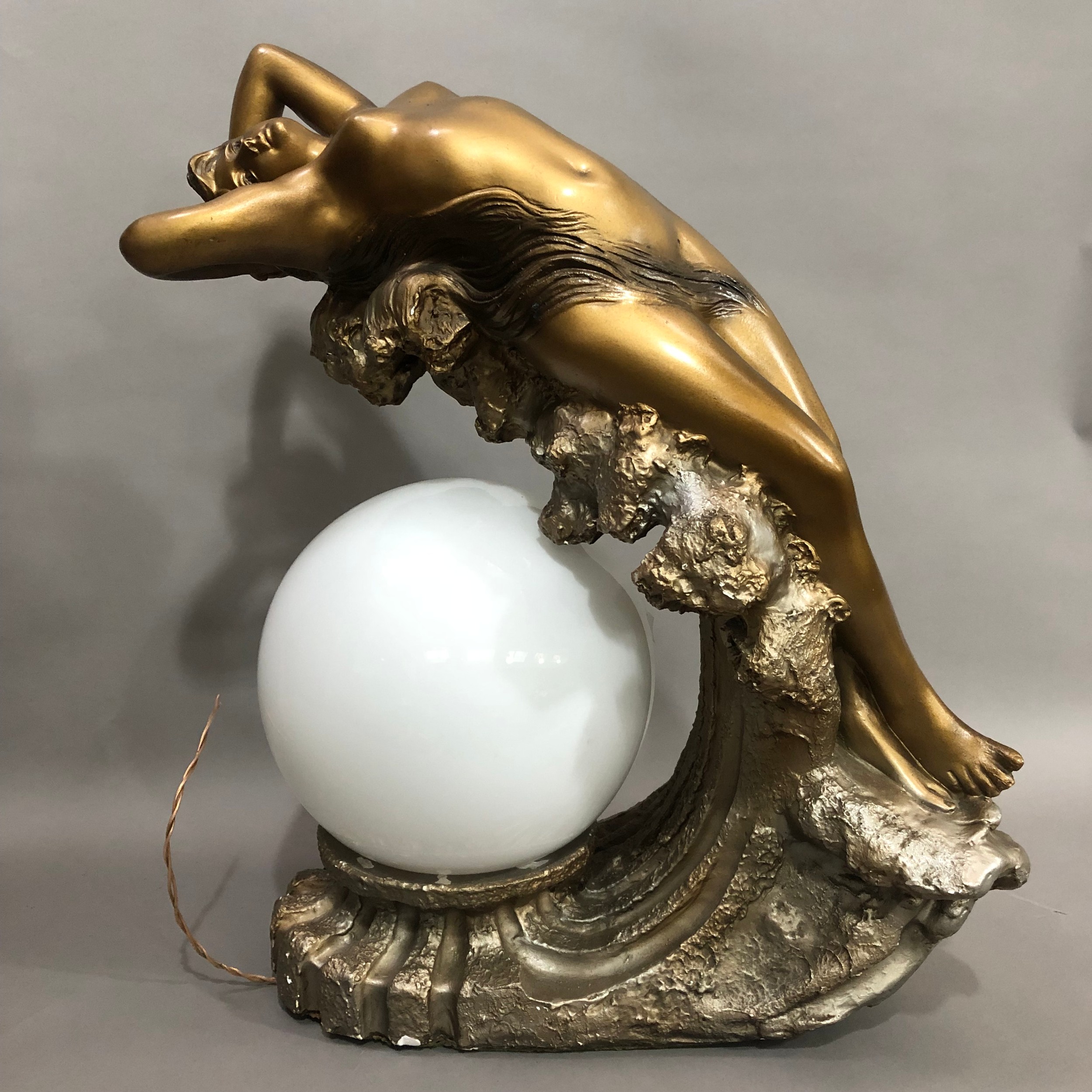 An Art Deco gilded plaster table lamp modelled as a nude female reclining on the crest of a wave