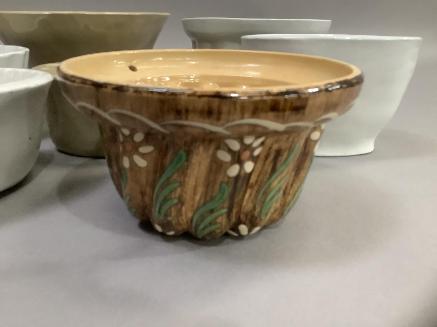 Seven white and buff pottery jelly moulds and one painted with leaves and flower heads on a brown - Image 2 of 2