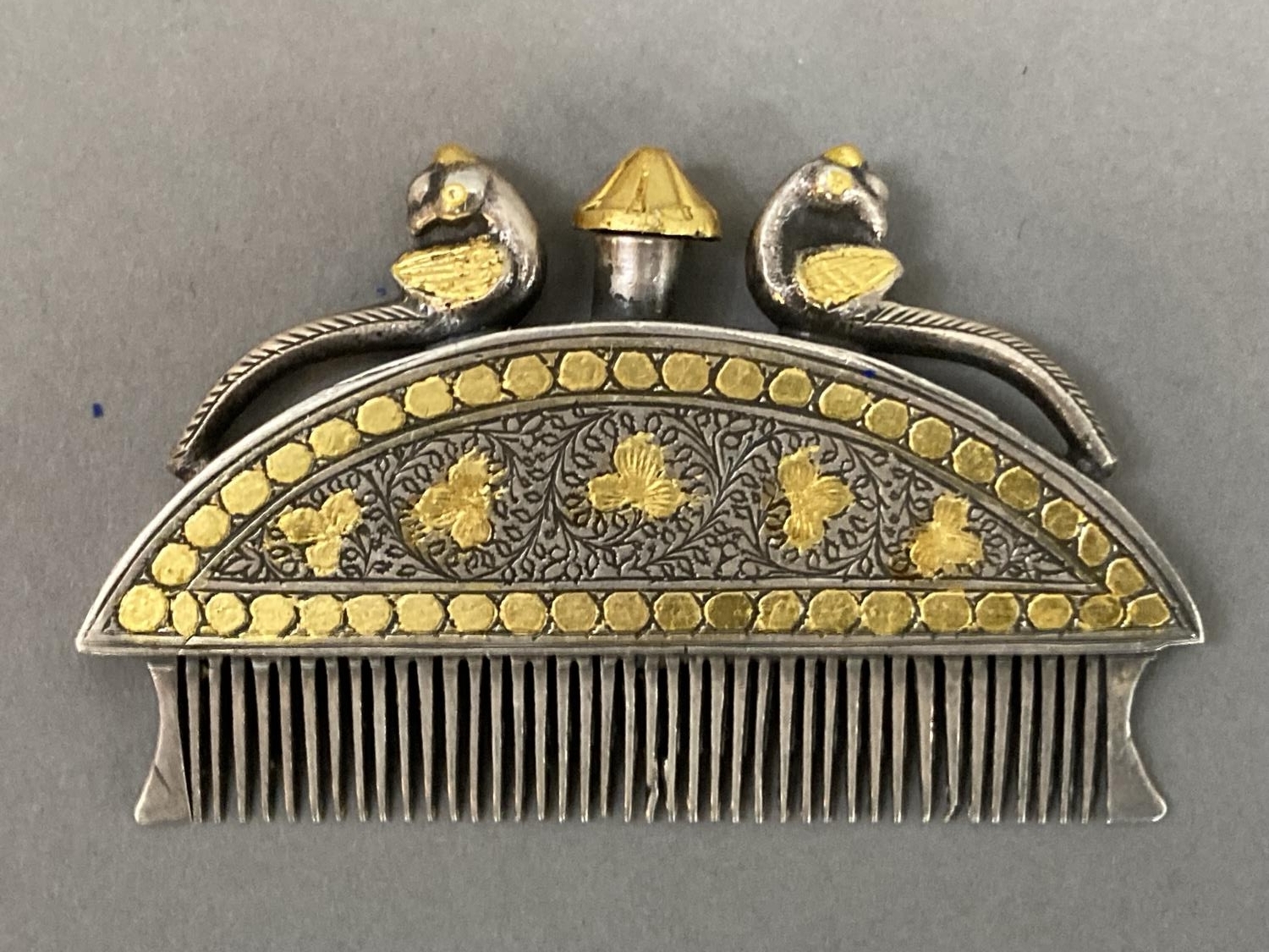 An Indian, white metal moustache comb with gilt metal inlay, the finial, surmounted by two peacocks, - Image 2 of 2