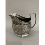 A George III silver helmet cream jug chased with a band of scrolling flower heads between fluted