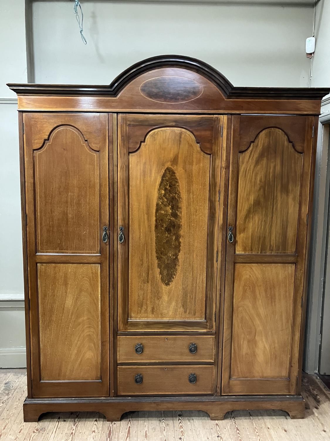 An Edwardian three door wardrobe of semi arched profile with moulded cornice, the middle door having