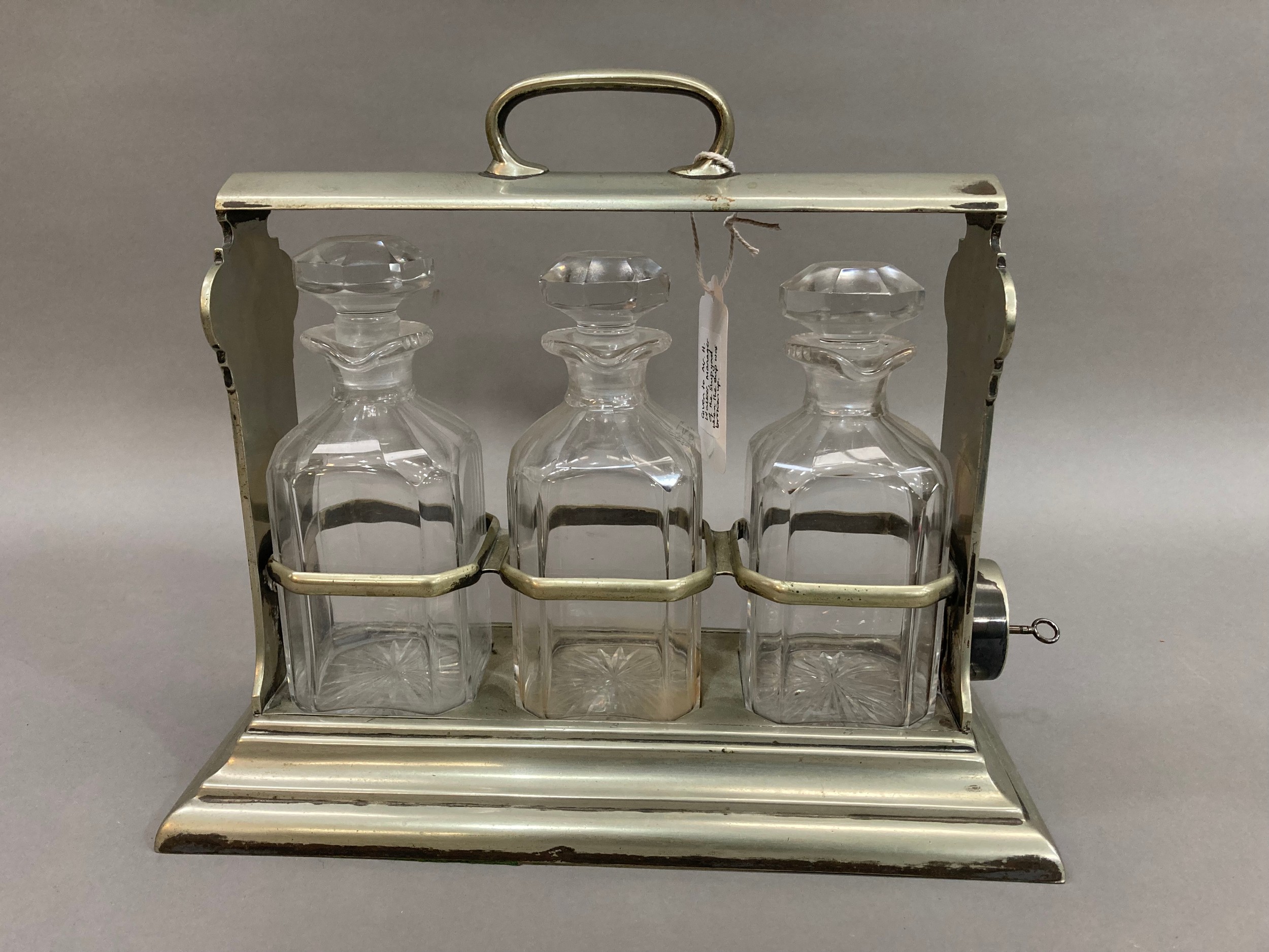 A silver plated tantalus fitted with three glass decanters of square outline from R M S Berengaria