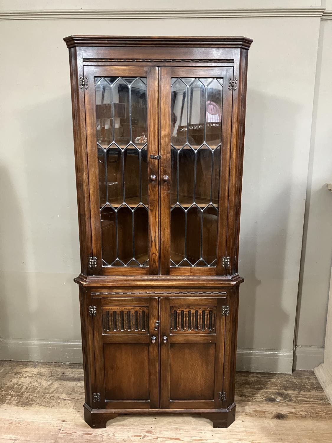 A Reprodux standing corner cupboard having a moulded cornice above leaded glazed two door cupboard