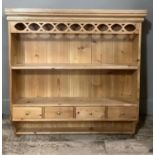 A pine hanging shelf with carved frieze, middle shelf above four small drawers and shelf below