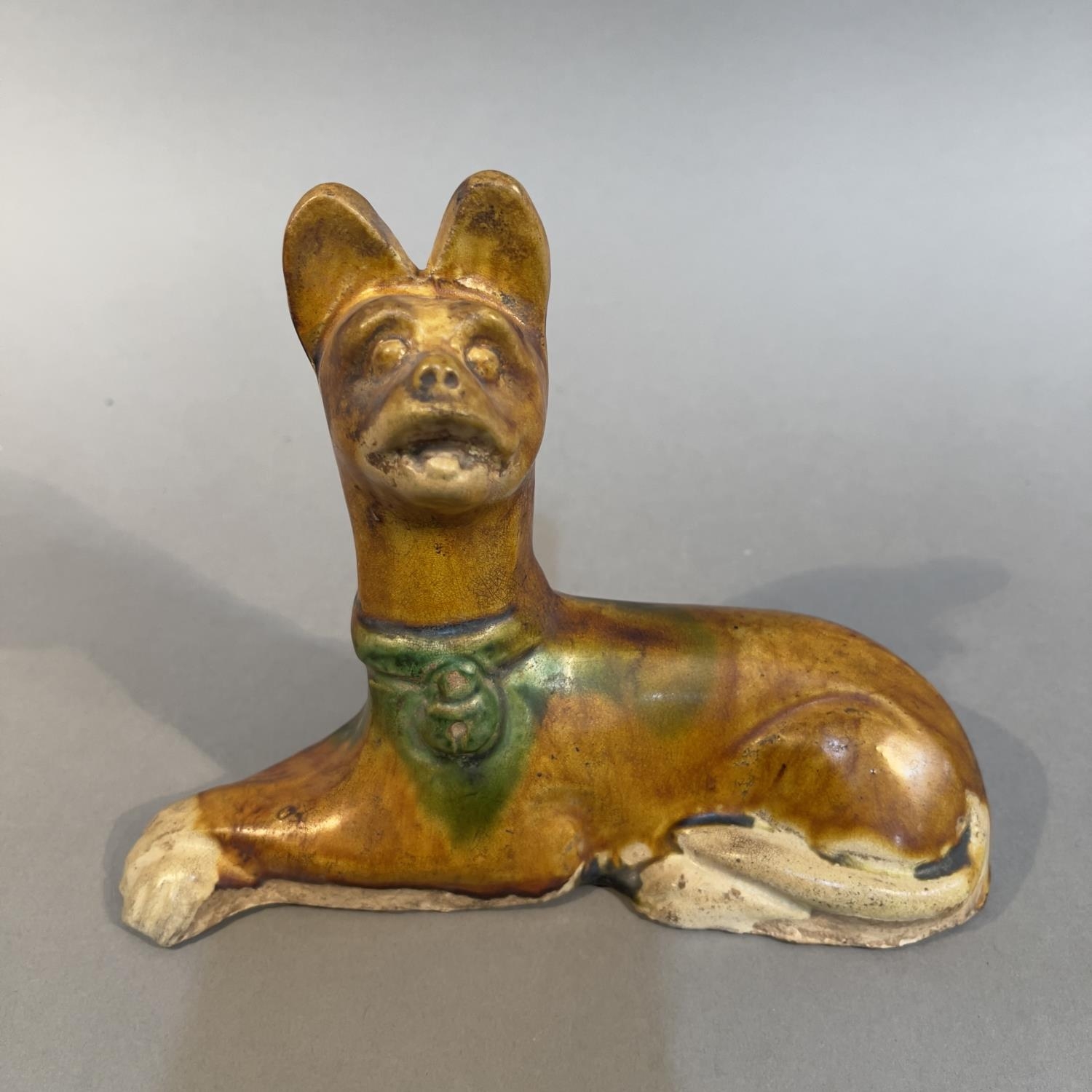 A Tang-style Sancai glazed pottery figure of a recumbent dog 18cm wide x 14cm high (Shipping