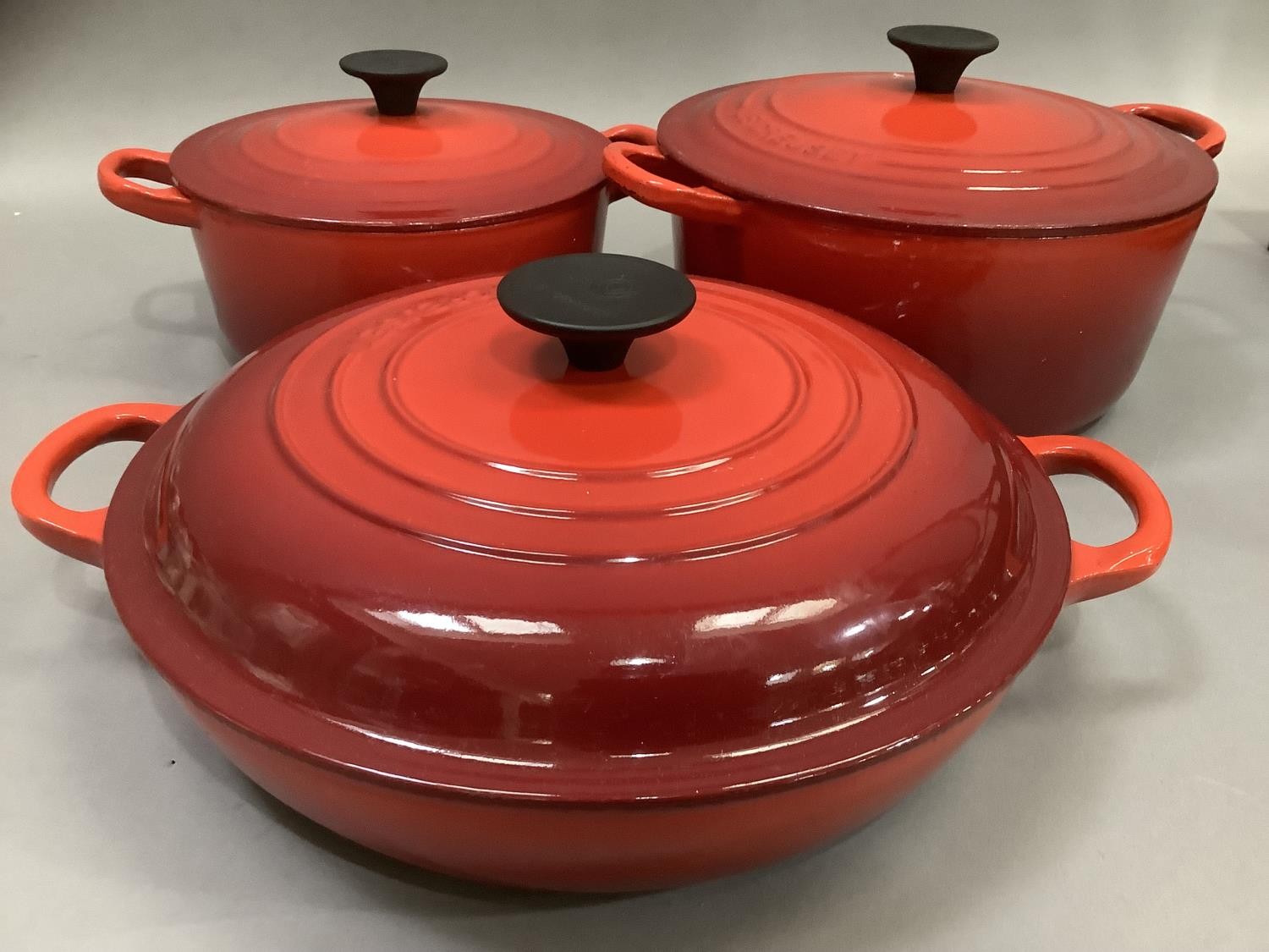 A set of three Le Creuset two handled casseroles in flame red, with lids, as new, 19cm, 22.5cm and a