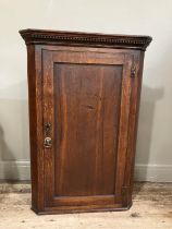 A 19th century oak corner hanging cupboard with moulded and dentil cornice above an indented panel