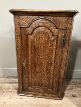 A 19th century oak corner hanging cupboard having moulded cornice above semi arched panel door and