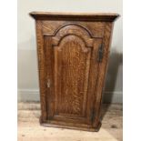 A 19th century oak corner hanging cupboard having moulded cornice above semi arched panel door and