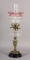 A Victorian brass oil lamp, clear glass reservoir, cranberry tinted opaque shade etched with