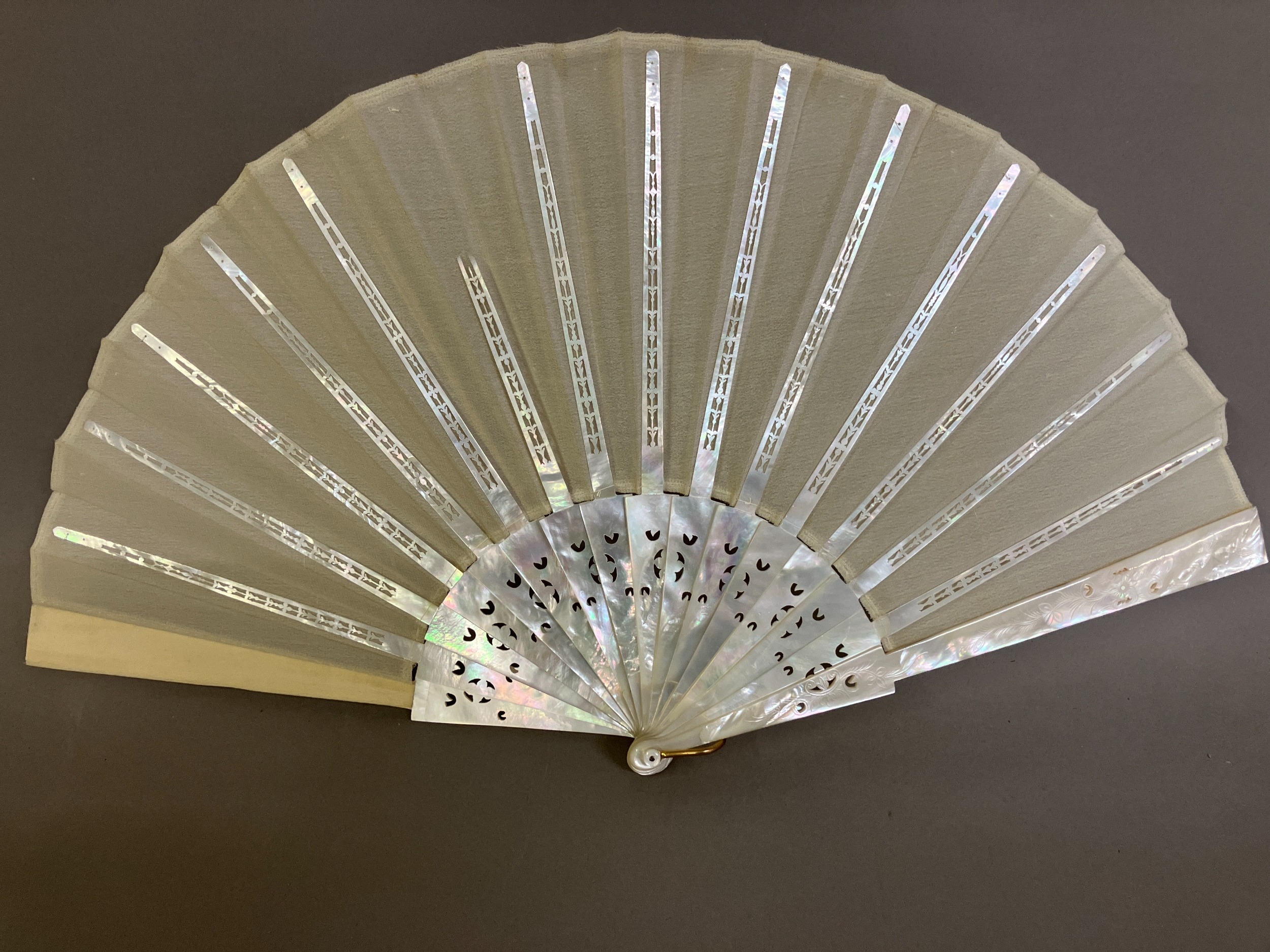 A white Mother of Pearl fan, with a hint of colour, the guards and gorge with decorative piercing