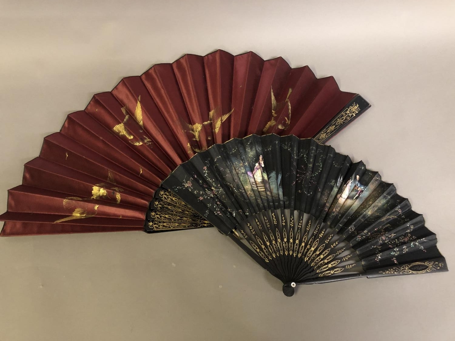 A black wood fan, carved and gilded, early 20th c, mounted with a silk leaf, painted with a courting