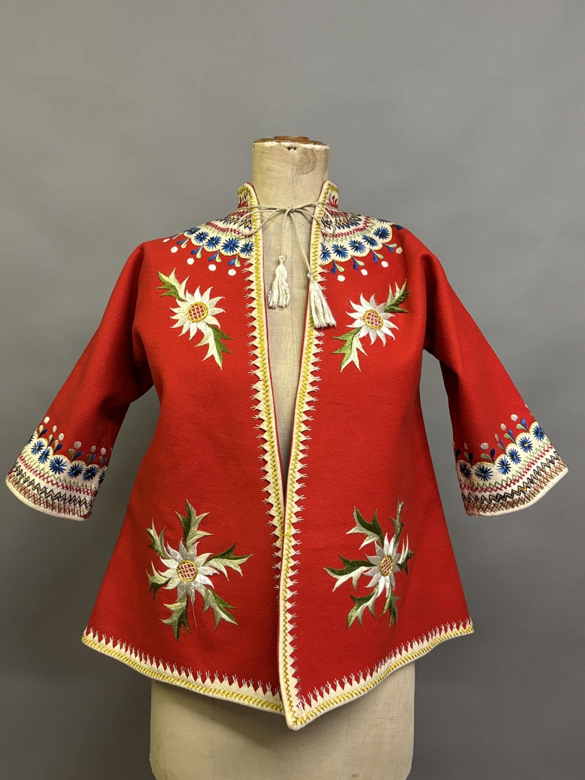 A Child’s folk dress coat, in red wool with cream cuffs, seam and collar, heavily embroidered with