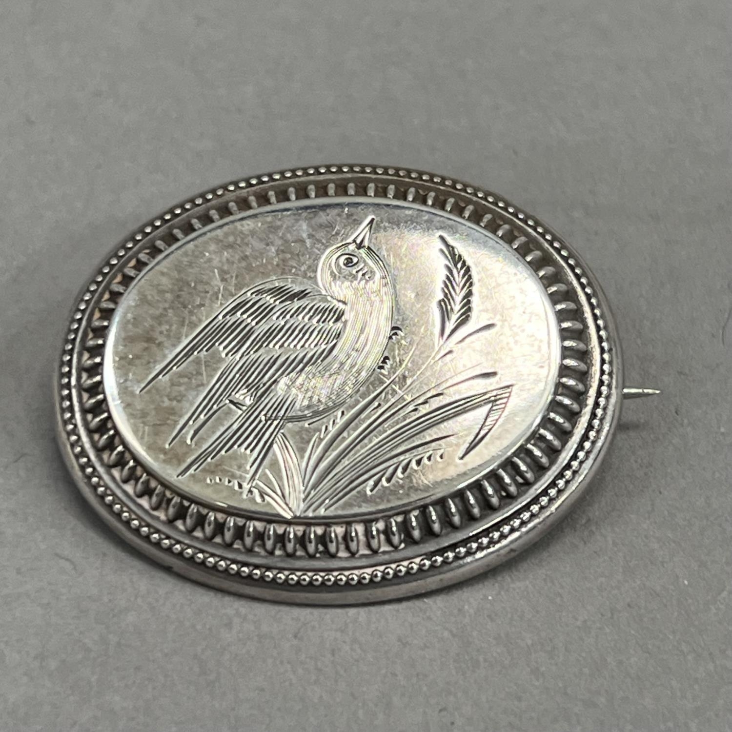 A Victorian oval silver brooch, engraved with a song bird perched in grasses raised against a - Image 2 of 2