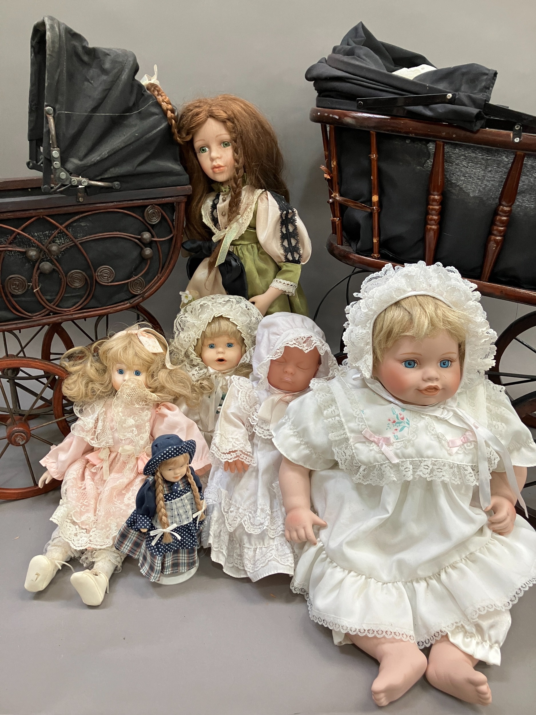 A collection of six modern porcelain dolls in costume, together with two Victorian style prams