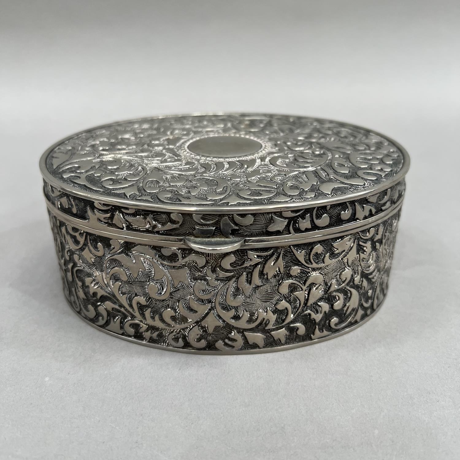 An oval box in white base metal with hinged lid, all over foliate chasing and an open circular - Image 2 of 3