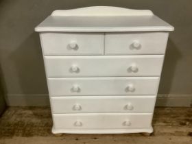 A modern off white chest of drawers having a short raised back above two short and four long drawers