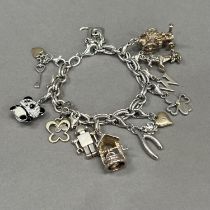 A silver bracelet of trace and jump ring links hung with silver charms variously set with enamel,