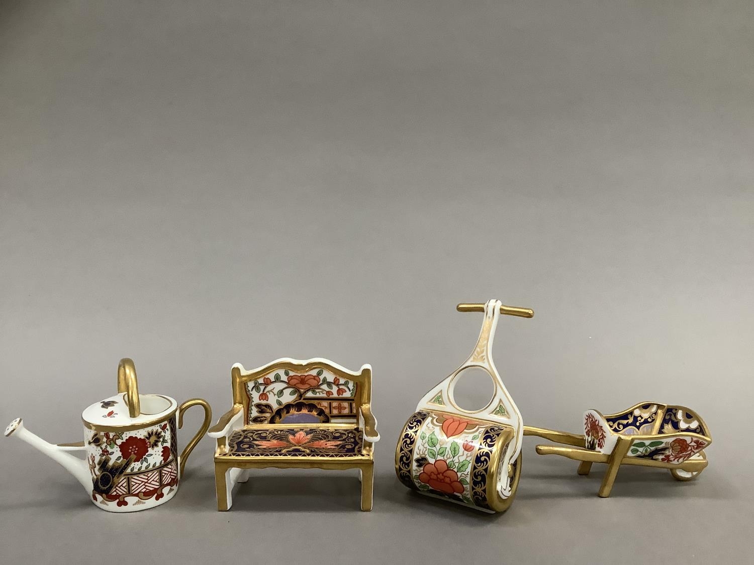 Four Royal Crown Derby miniatures including ag garden bench, watering can, wheelbarrow and garden