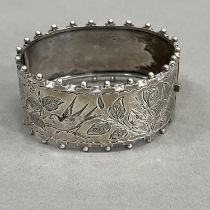 A Victorian silver stiff hinged bangle, engraved to the front with flora and fauna within beaded and