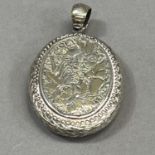 A Victorian oval silver locket foliate engraved to the front with an open shield cartouche and