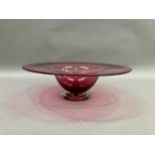 A contemporary cranberry glass bowl with broad flat and folded rim on a clear glass foot, 38cm