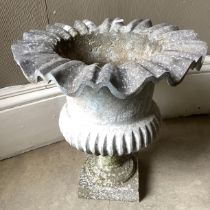 A composition garden urn having a frilled rim and lower reeded body, on pedestal foot with square
