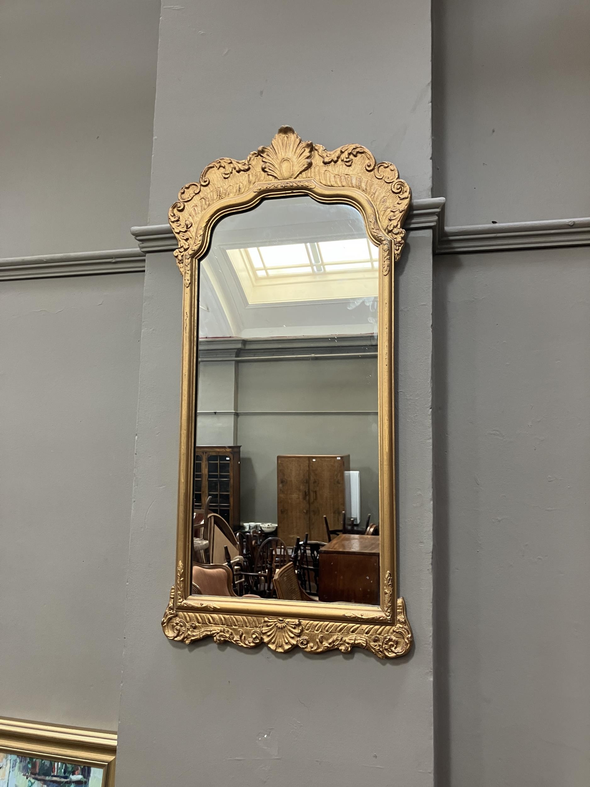 A gilt framed wall mirror of arched outline with foliate moulded pediment, 87cm x 45cm