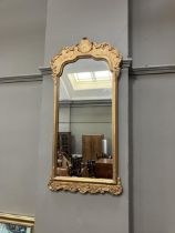 A gilt framed wall mirror of arched outline with foliate moulded pediment, 87cm x 45cm