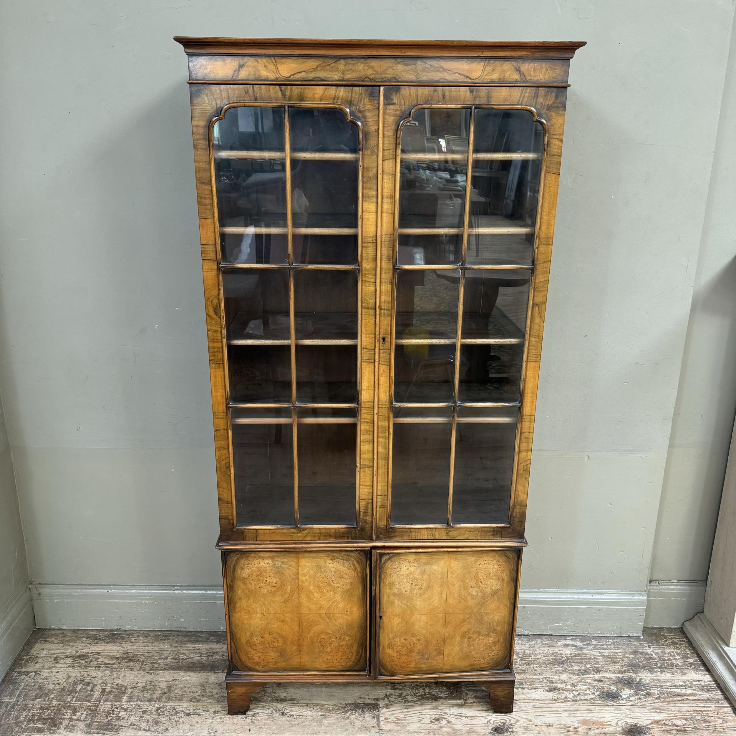 A mid 20th century walnut and glazed bookcase cupboard, having a moulded cornice above two tracery