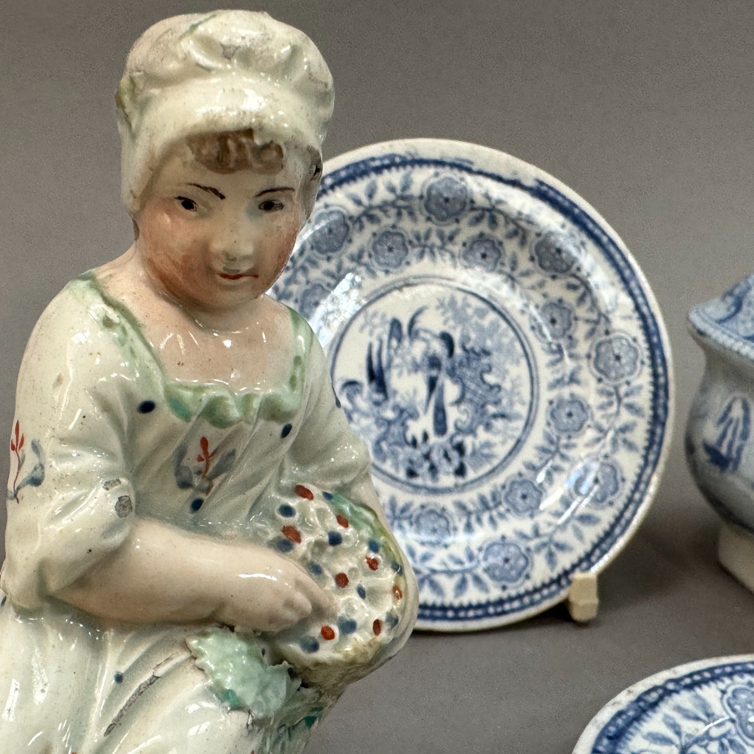 An early 19th century cream ware figure reclining on a rock with basket of fruit, on a cream - Image 2 of 3