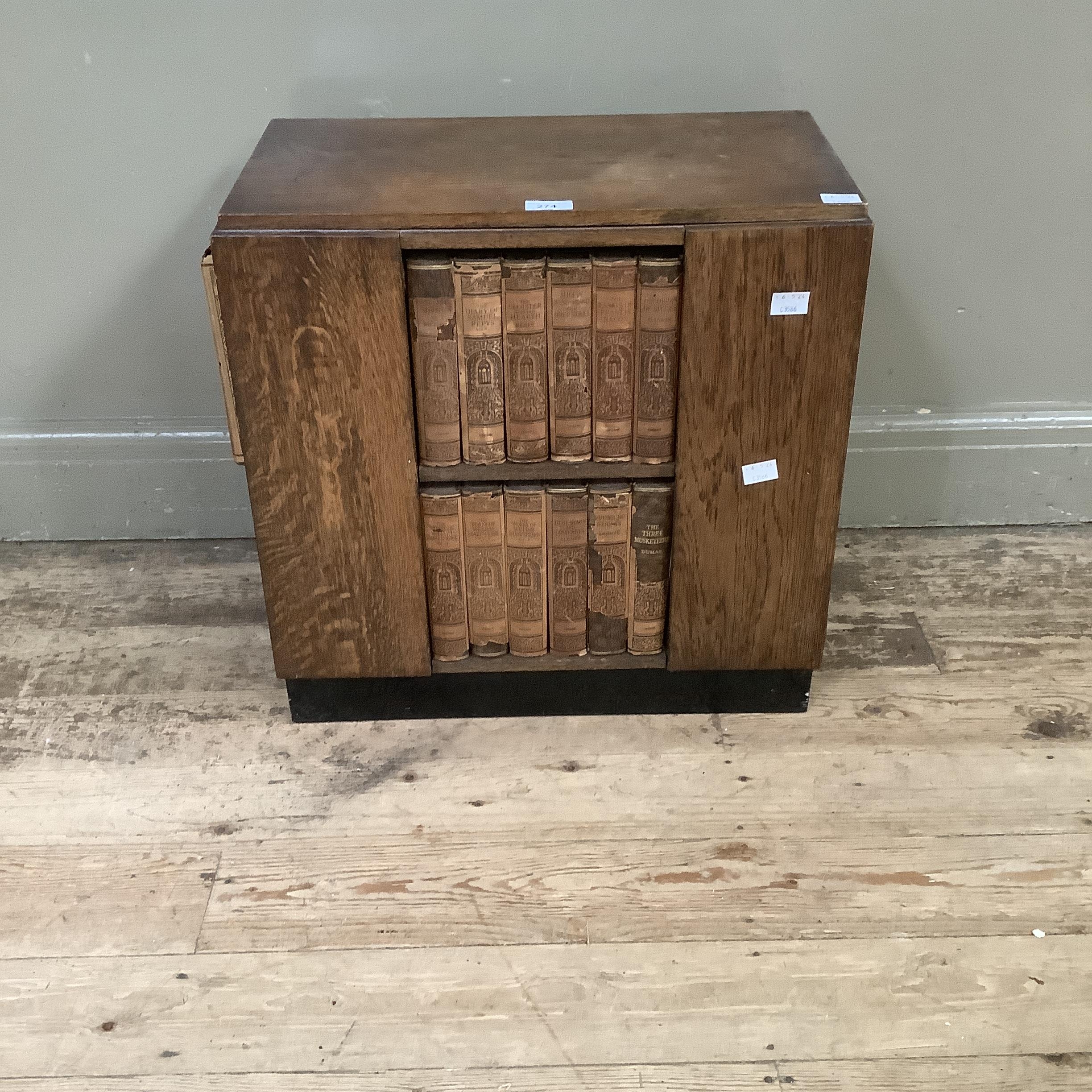 An art deco oak bookcase with compartments to each side on a plinth base and holding a set of